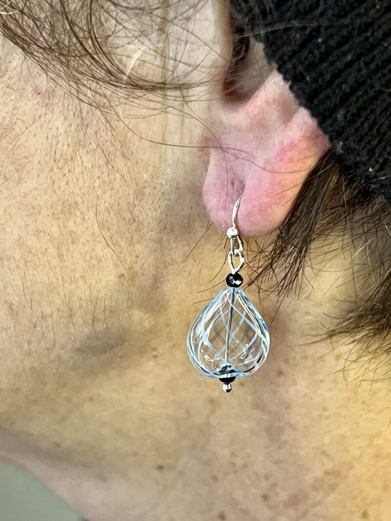 Øreringe med mundblæst glas perle i flad dråbe form i klar med lys blå striber. Vælg i mellem forgyldt / forsølvet, eller Sterling sølv / forgyldt. Længden er ca. 3.5cm Prisen er for et par øreringe.