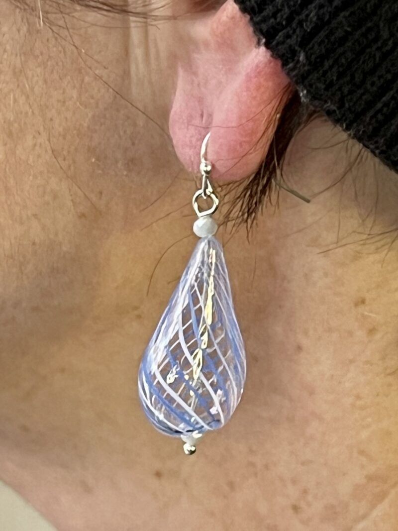 Øreringe med mundblæst glas perle i flad dråbe form i lys blå med hvide og blå  striber. Vælg i mellem forgyldt / forsølvet, eller Sterling sølv / forgyldt. Længden er ca. 5,7cm. Prisen er for et par øreringe.